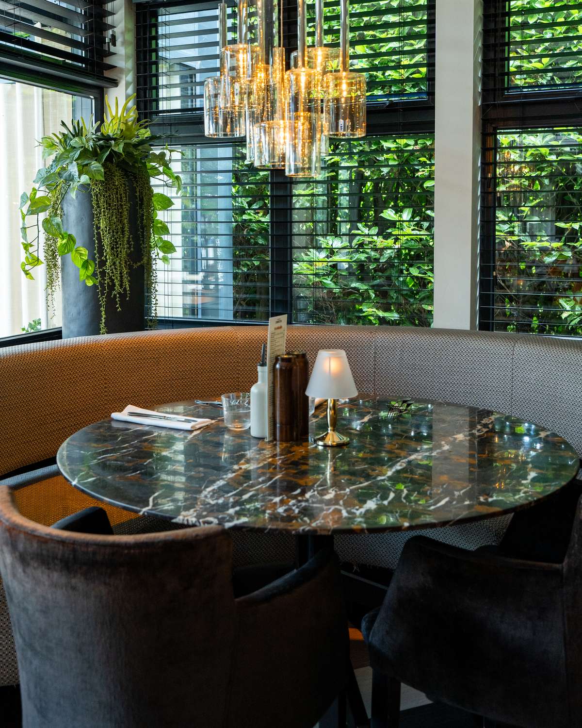 Een ronde marmeren tafel in de zitbank bij het raam, met een brandend tafellampje en groen buiten
