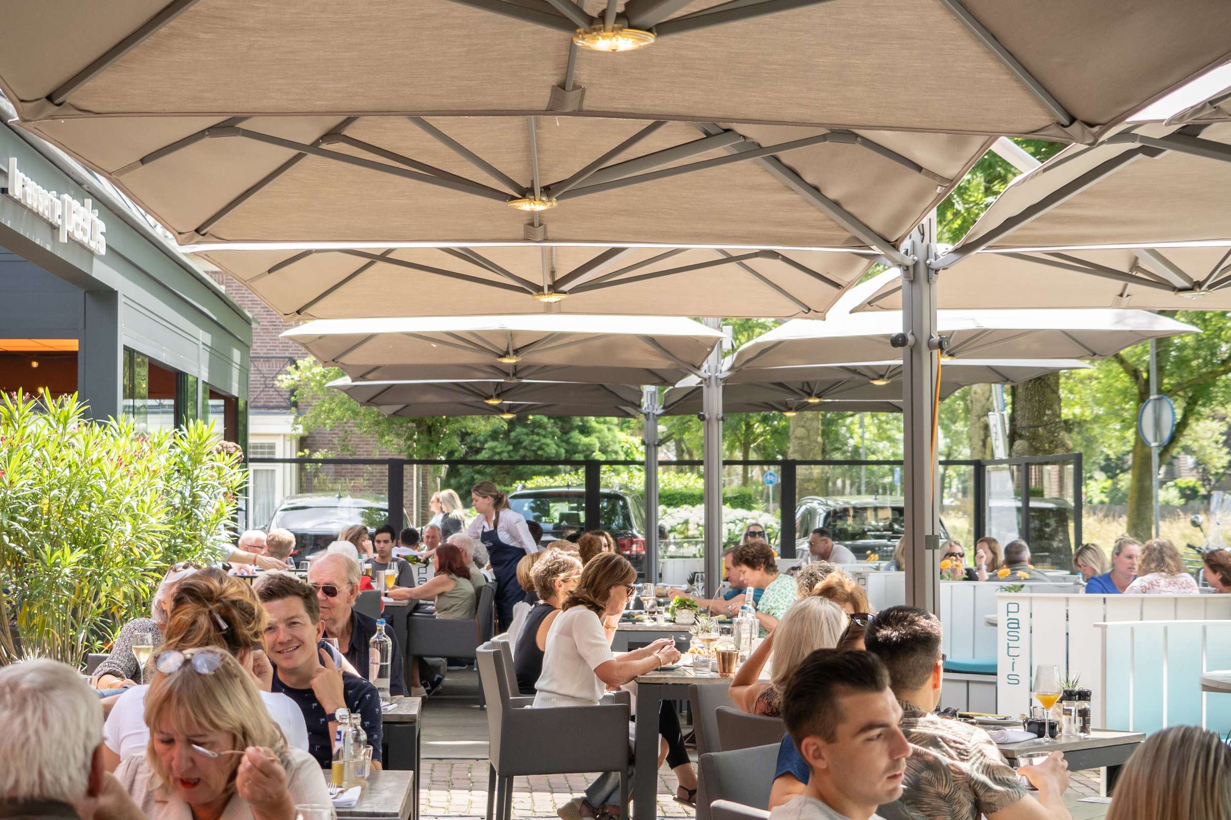 Het volle terras van Brasserie Pastis in Rosmalen op een zomerdag, onder de vaste parasols